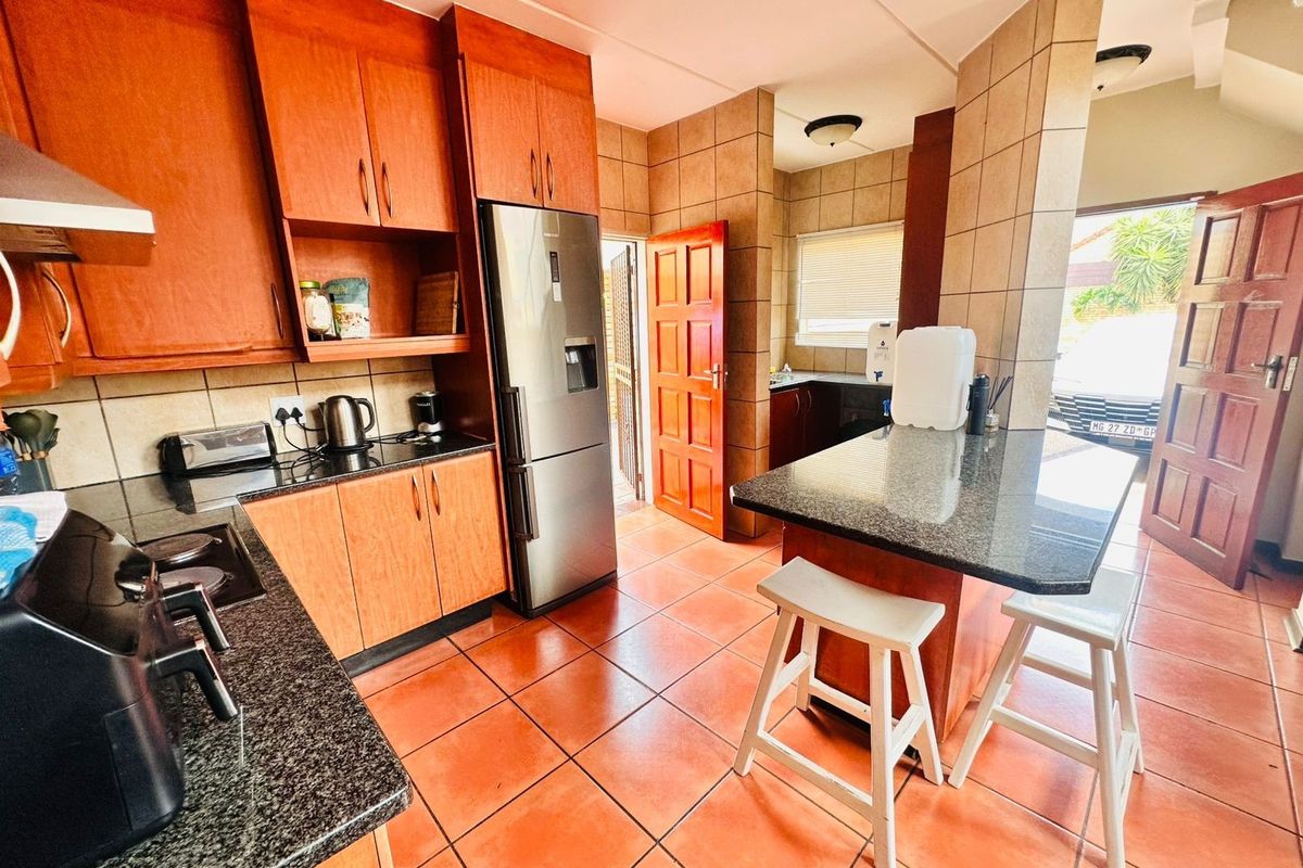 A functional kitchen featuring granite countertops, wooden cabinetry, tiled flooring, and a breakfast bar, with direct access to the exterior.