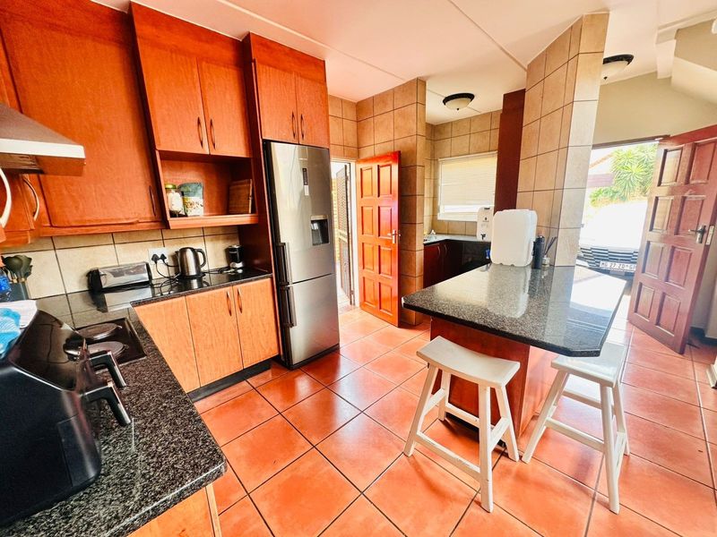 A functional kitchen featuring granite countertops, wooden cabinetry, tiled flooring, and a breakfast bar, with direct access to the exterior.