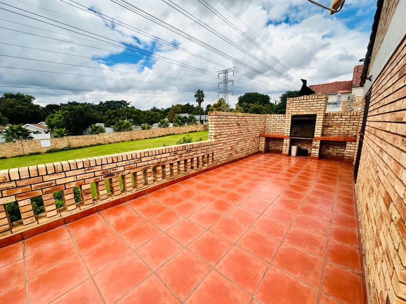 Spacious outdoor patio featuring a built-in brick braai, tiled flooring, and a decorative brick balustrade overlooking the garden area.