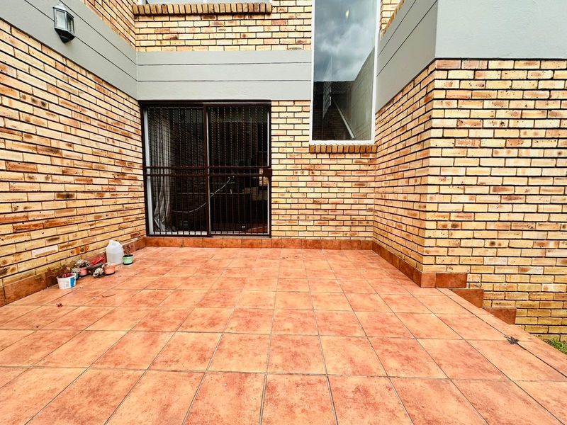 A private outdoor patio area featuring face brick walls, tiled flooring, and a secure sliding door entrance.