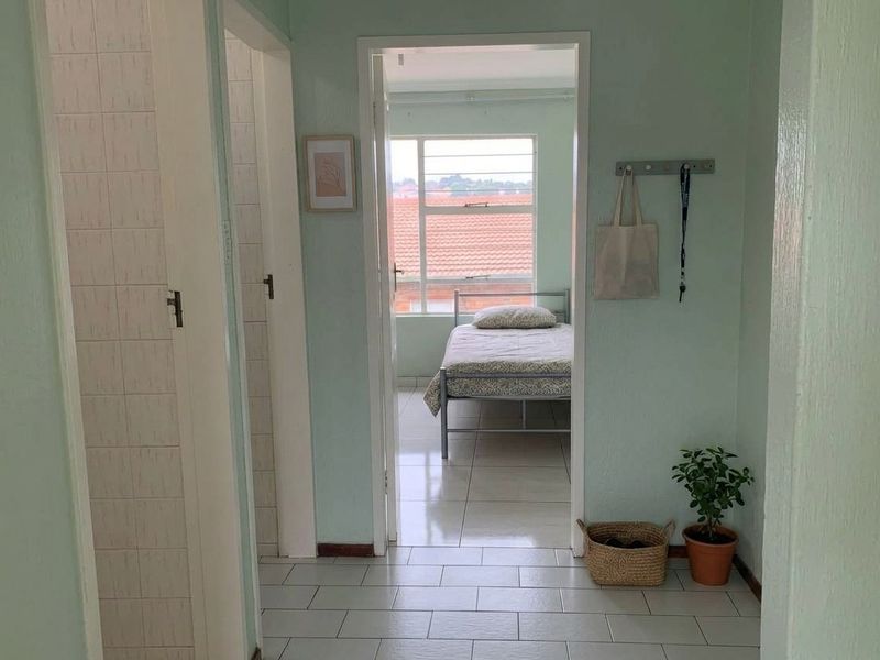 A functional hallway with tiled flooring providing access to adjacent rooms, including a bedroom with natural light.