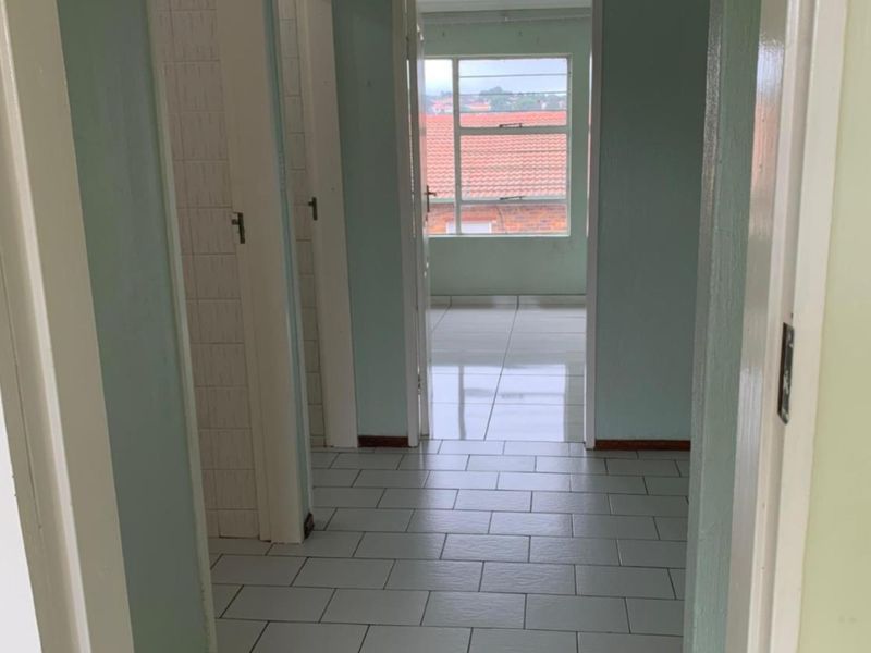 A vacant hallway with tiled flooring leading to an adjacent room with a window, featuring dated paintwork and standard internal door frames.