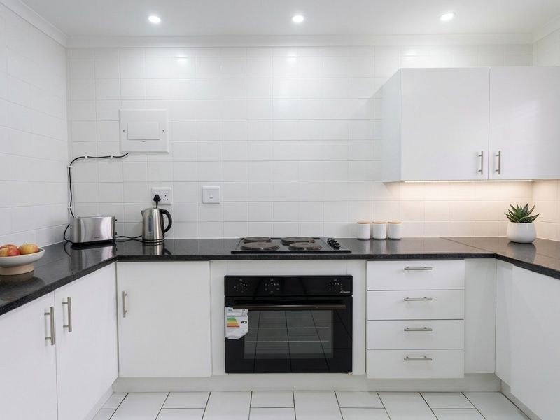 A modern, well-maintained kitchen featuring white cabinetry, black granite countertops, a built-in oven, electric hob, and clean tiled finishes.