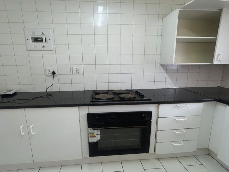 A functional kitchen featuring built-in oven, electric hob, granite countertops, and white cabinetry, currently in need of cosmetic updates.