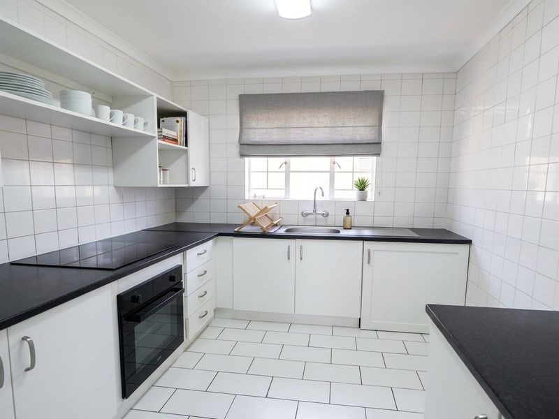 A clean, well-maintained kitchen featuring white cabinetry, black countertops, built-in oven, electric cooktop, and tiled finishes throughout.