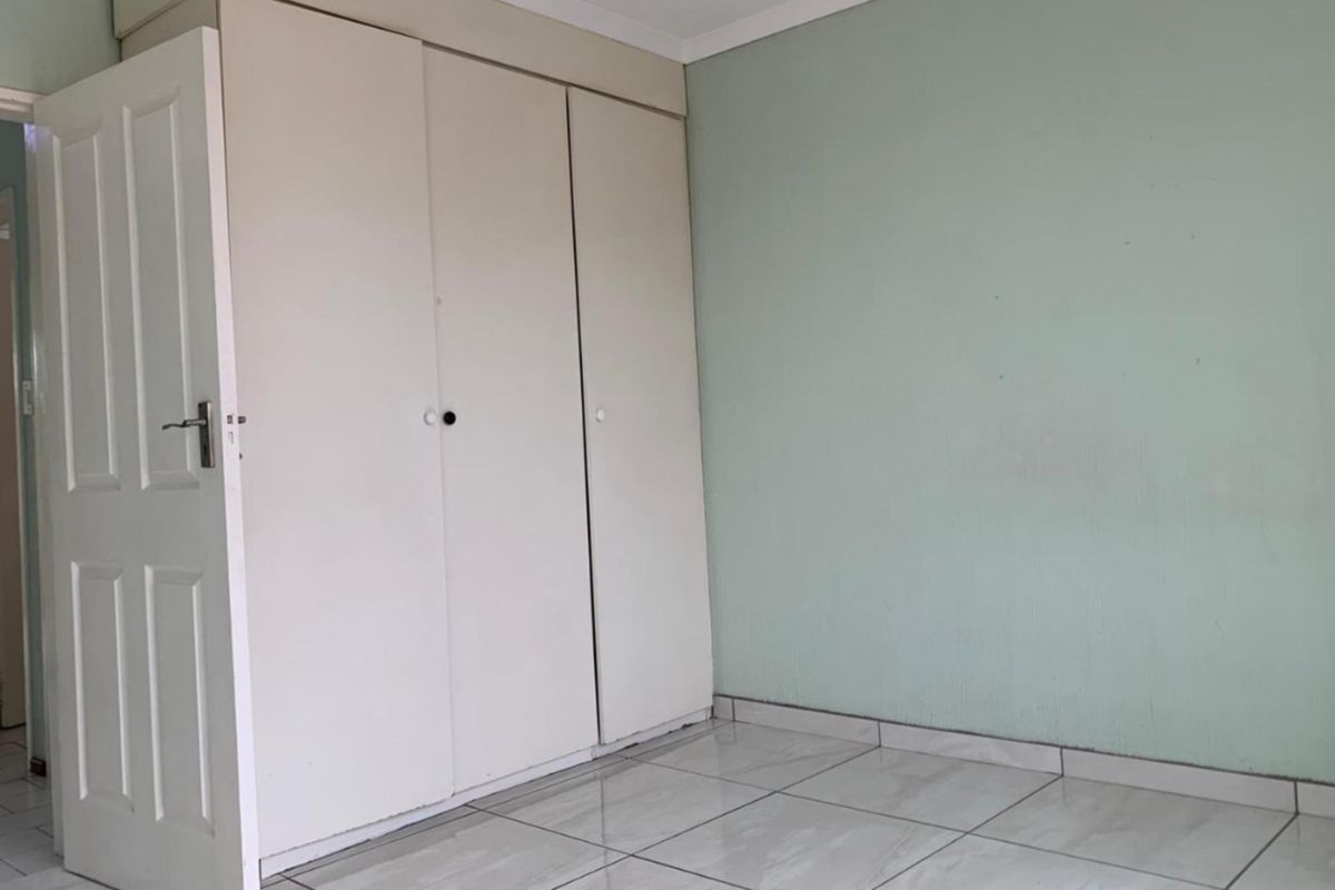 An empty bedroom featuring neutral tiled flooring and built-in cupboards, providing a blank canvas for personalization.