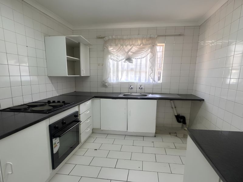 A functional kitchen featuring built-in cabinetry, a black laminate countertop, an electric oven and hob, and a stainless steel sink with tiled finishes.