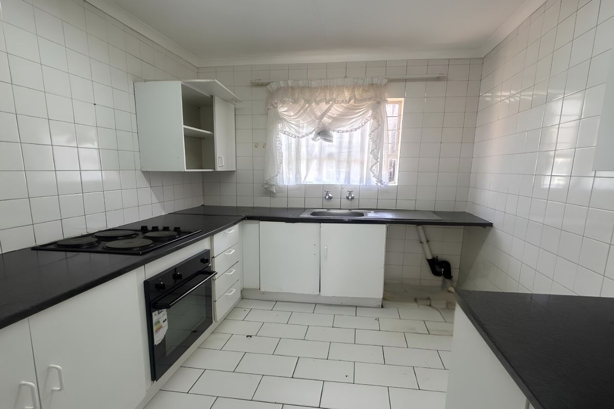 A functional kitchen featuring built-in cabinetry, a black laminate countertop, an electric oven and hob, and a stainless steel sink with tiled finishes.