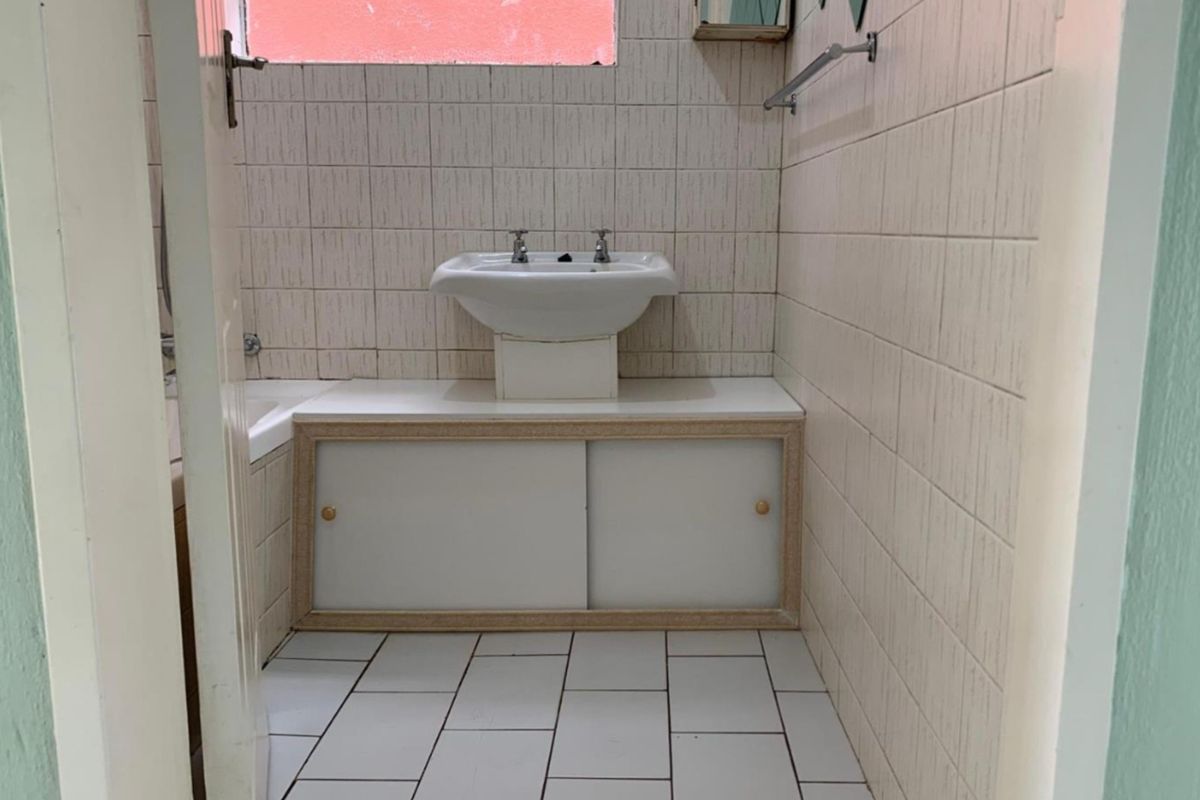 A compact bathroom featuring a pedestal washbasin, built-in vanity storage, and full-height wall tiling.