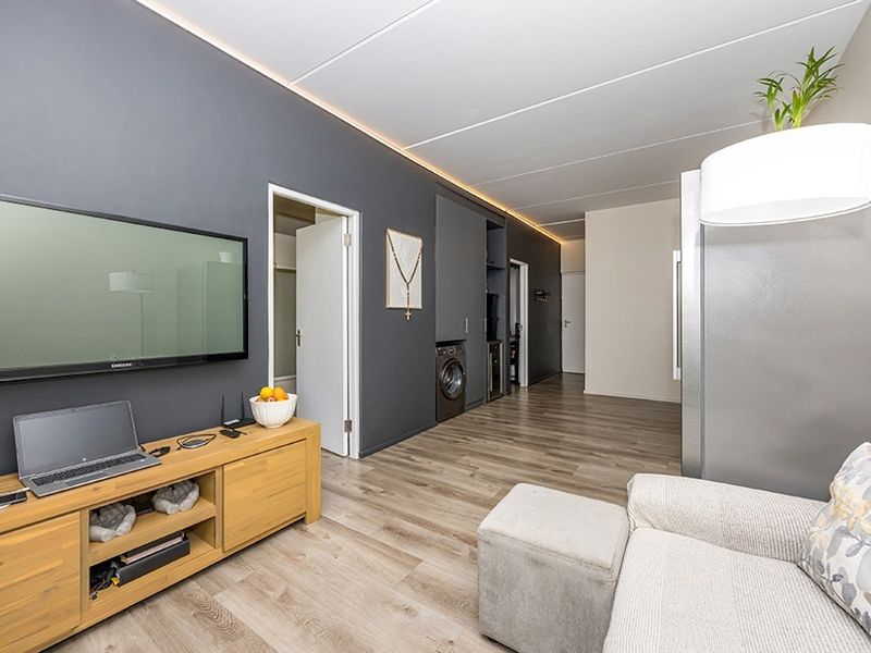 Modern open-plan living area featuring laminate flooring, recessed ceiling lighting, and sleek built-in cabinetry with an integrated laundry space.