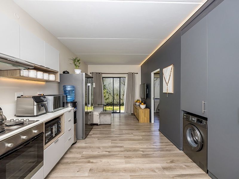 Modern open-plan kitchen and living area featuring sleek cabinetry, integrated appliances, wood-look flooring, and direct access to an outdoor patio space.