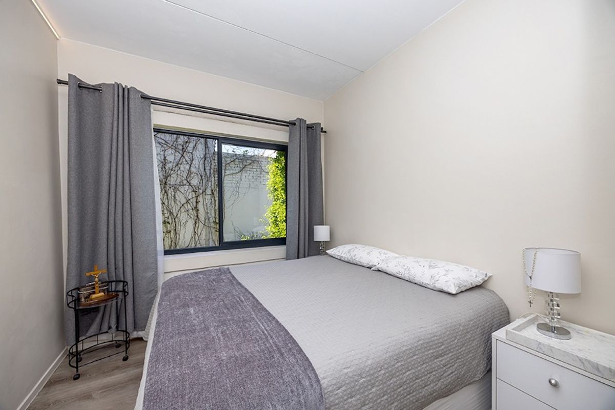 A well-maintained bedroom featuring neutral walls, laminate flooring, and a sliding window with integrated curtain rod.