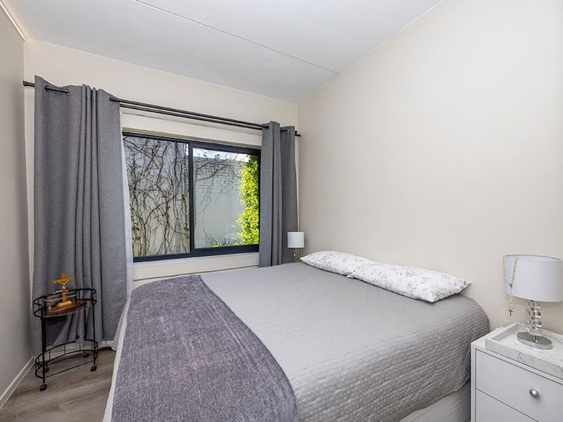 A well-maintained bedroom featuring neutral walls, laminate flooring, and a sliding window with integrated curtain rod.