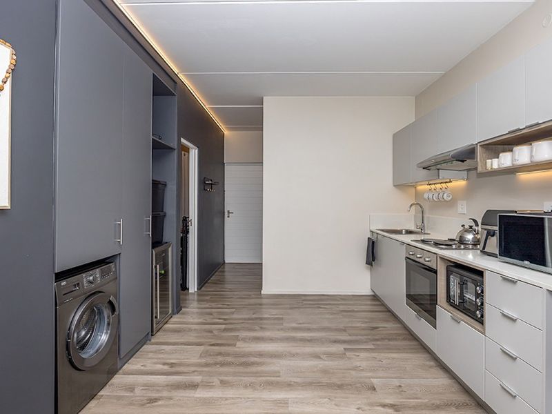 Modern galley-style kitchen featuring sleek grey cabinetry, integrated appliances, wood-look laminate flooring, and efficient recessed lighting.