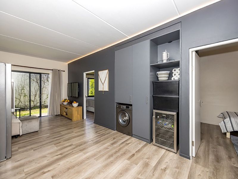 Modern open-plan living area featuring sleek grey built-in cabinetry with integrated laundry and wine cooling facilities, laminate flooring, and access to a private patio.