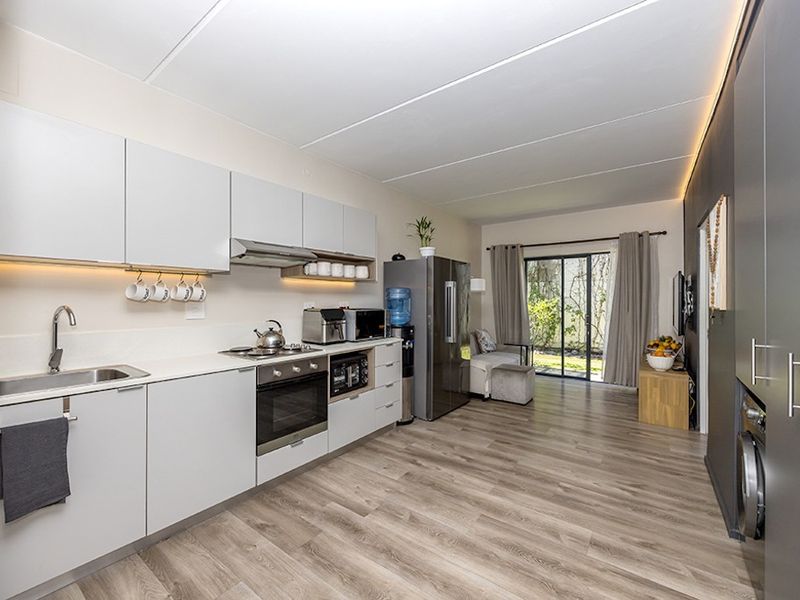Modern open-plan kitchen and living area featuring sleek cabinetry, integrated appliances, laminate flooring, and direct access to an outdoor space through sliding glass doors.