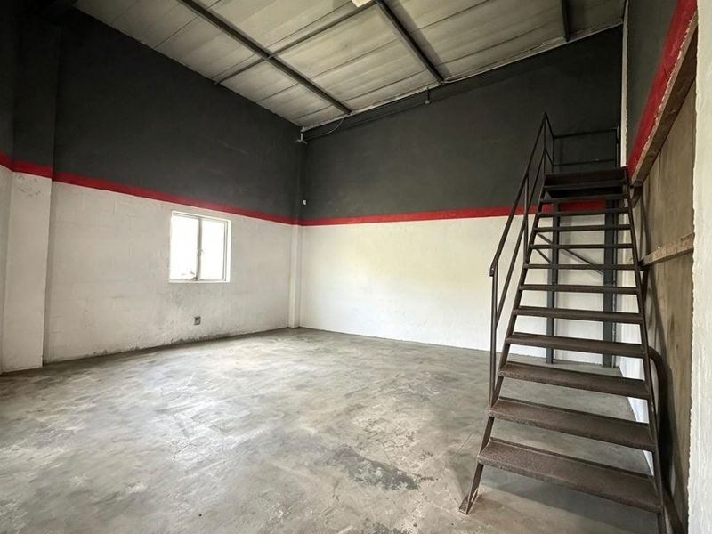 An empty industrial utility space featuring high ceilings with exposed beams, concrete flooring, and a fixed metal staircase leading to an upper level.