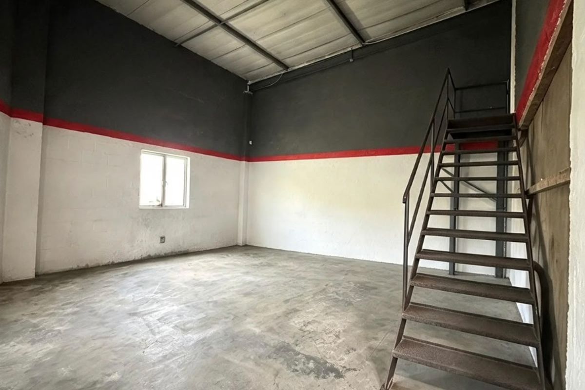 An empty industrial utility space featuring high ceilings with exposed beams, concrete flooring, and a fixed metal staircase leading to an upper level.