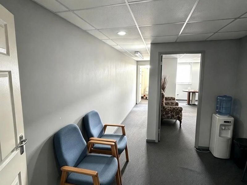 A functional commercial hallway featuring a suspended ceiling with recessed lighting and carpeted flooring, providing access to adjacent office spaces.