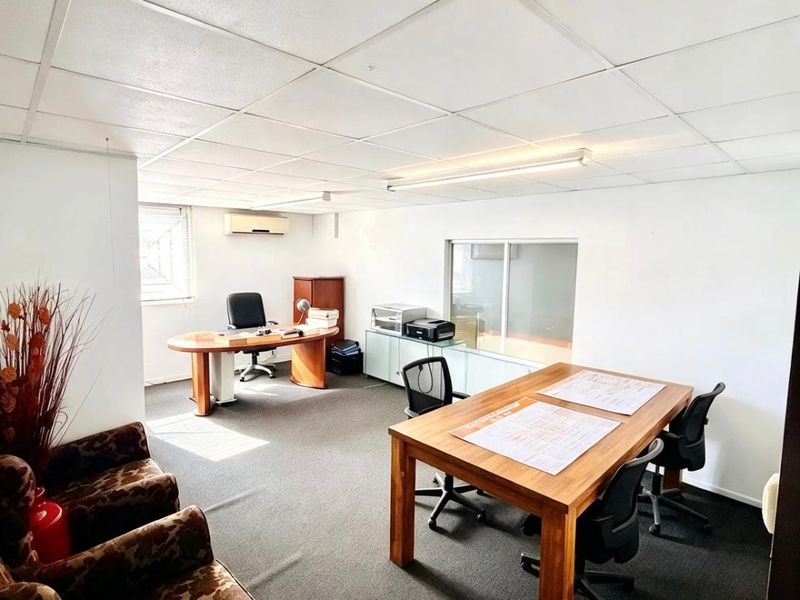 A functional commercial office space featuring a suspended ceiling, carpeted flooring, and a wall-mounted split-system air conditioning unit.