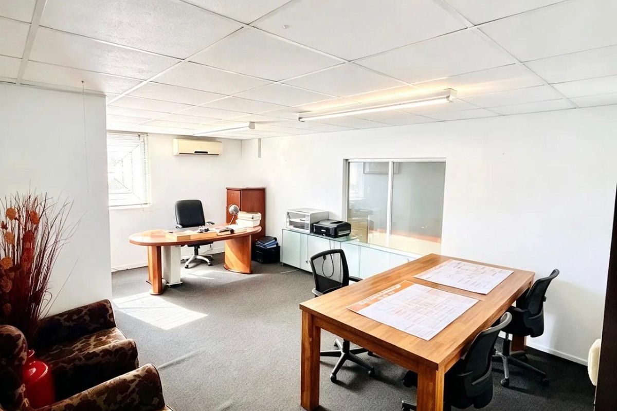 A functional commercial office space featuring a suspended ceiling, carpeted flooring, and a wall-mounted split-system air conditioning unit.