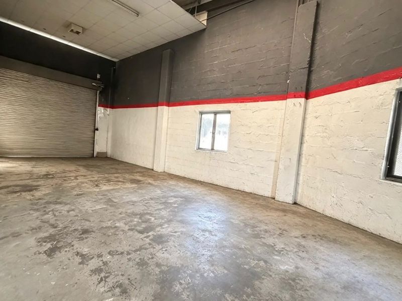 Spacious commercial utility or warehouse space featuring high ceilings, concrete flooring, and a large roller shutter door for easy access.