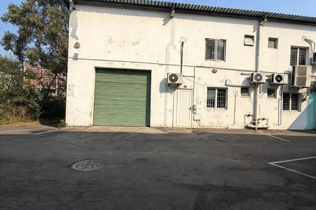 Rear exterior view of a commercial building featuring a roller shutter door, asphalt parking area, and multiple external air conditioning units.