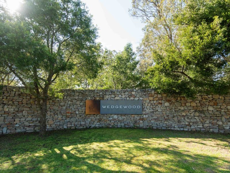 A well-maintained stone boundary wall featuring the Wedgewood estate signage, set against a backdrop of mature trees and landscaped greenery.