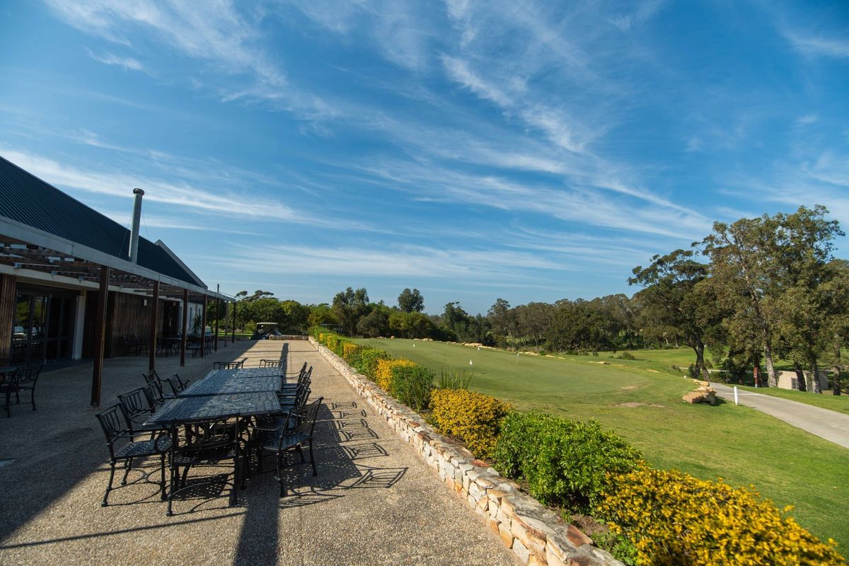 Spacious covered patio featuring exposed aggregate flooring and a stone retaining wall, overlooking a scenic golf course landscape.