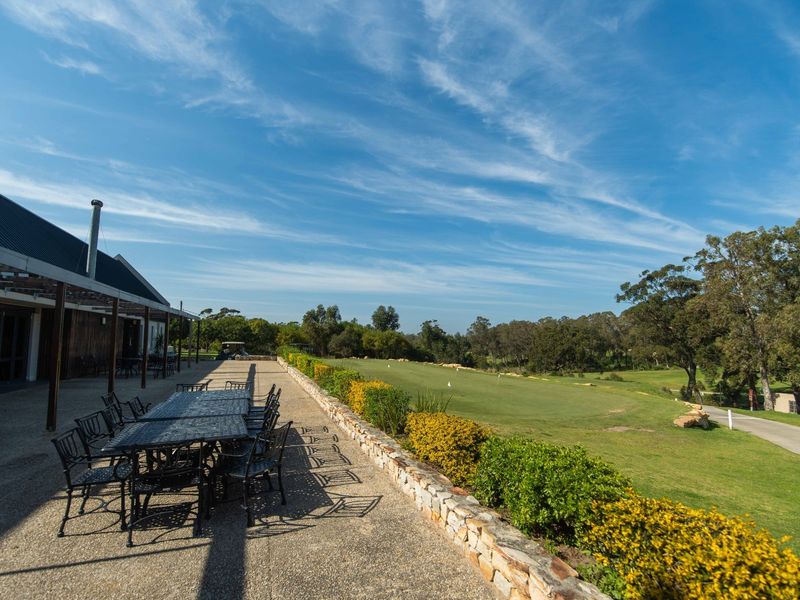 Spacious covered patio featuring exposed aggregate flooring and a stone retaining wall, overlooking a scenic golf course landscape.