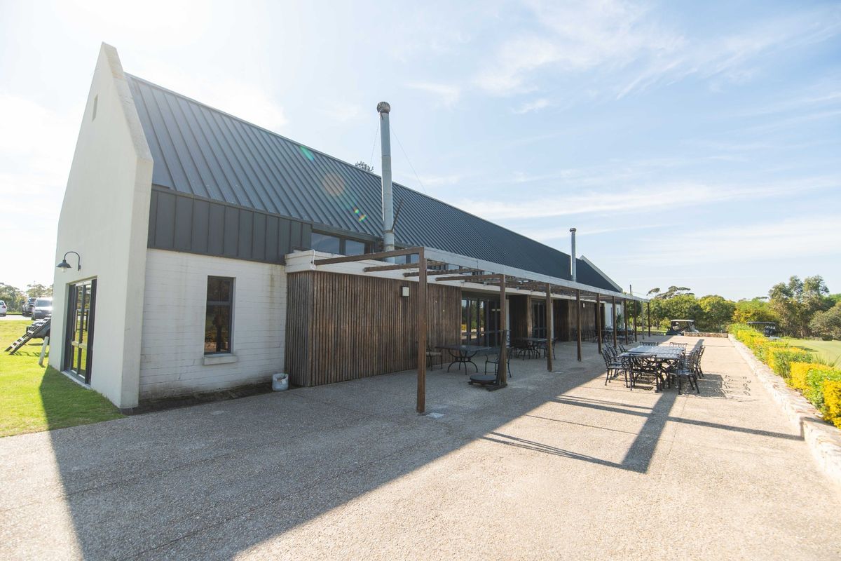Rear view of the property featuring a spacious concrete patio, timber-clad facade, and a modern metal roof with external flue pipes.