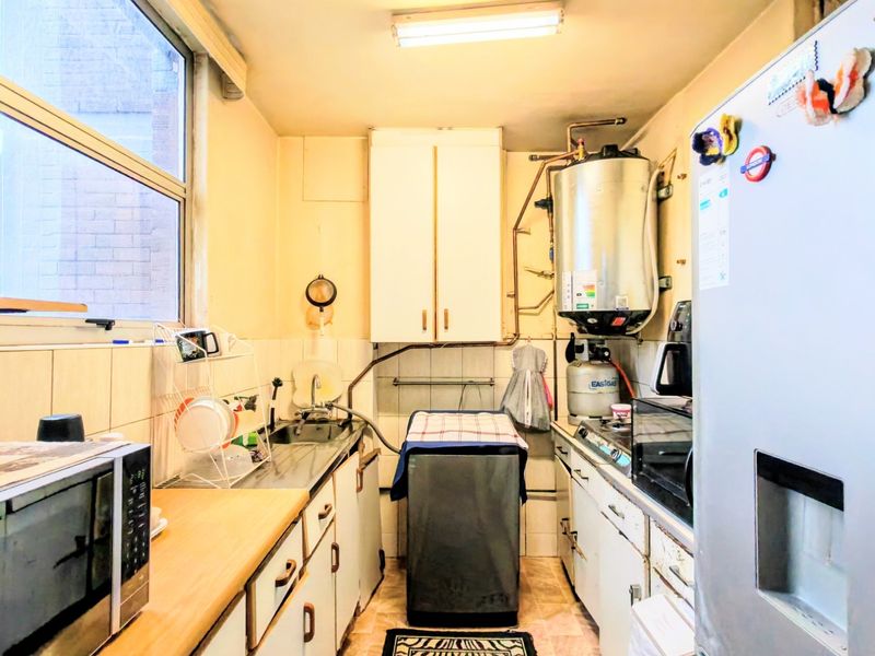 Compact kitchen featuring built-in cabinetry, stainless steel sink, gas hob, and an exposed gas geyser system.