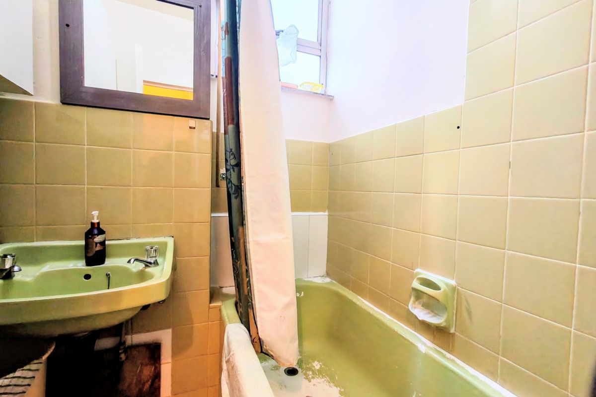A dated bathroom featuring a vintage green basin and bathtub, ceramic wall tiling, and a window, requiring modernization of fixtures and finishes.