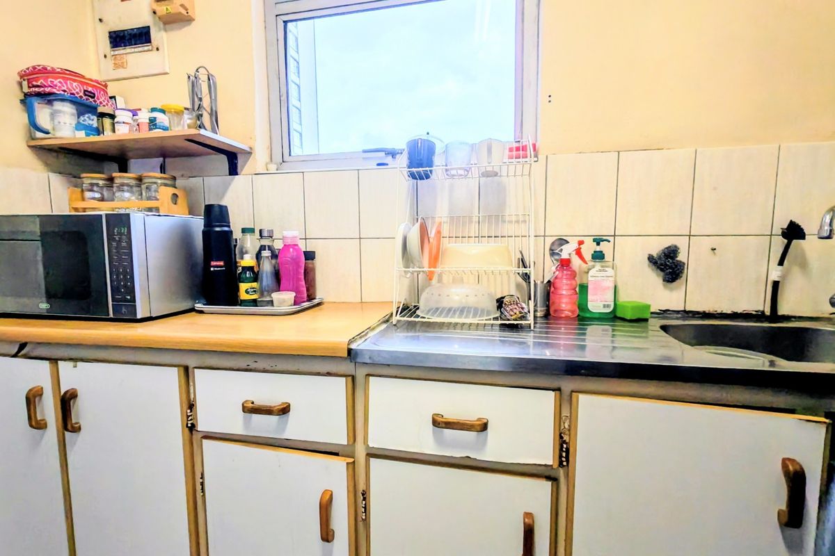 A functional kitchen area featuring laminate countertops, a stainless steel sink, tiled backsplash, and original built-in cabinetry in need of cosmetic updates.