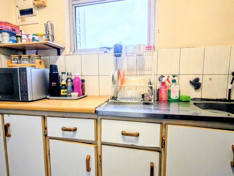 A functional kitchen area featuring laminate countertops, a stainless steel sink, tiled backsplash, and original built-in cabinetry in need of cosmetic updates.
