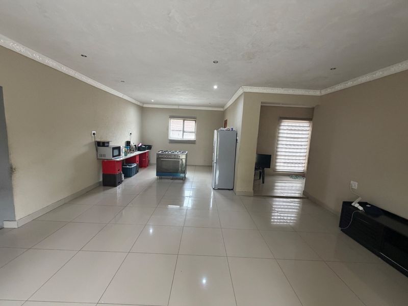 Spacious open-plan living and kitchen area featuring tiled flooring, recessed lighting, and crown molding, offering a blank canvas for renovation.