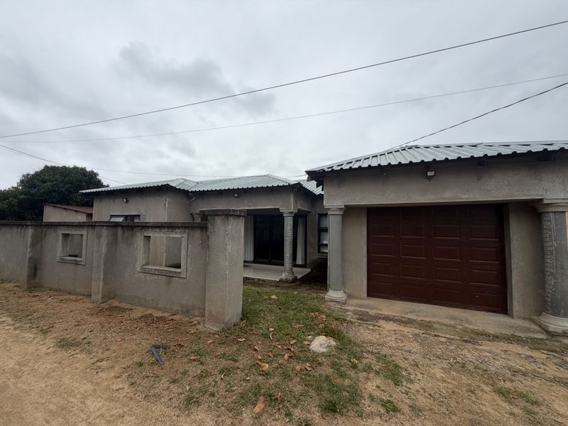 Front exterior view of a single-story house featuring a corrugated metal roof, concrete boundary wall, and an integrated garage.