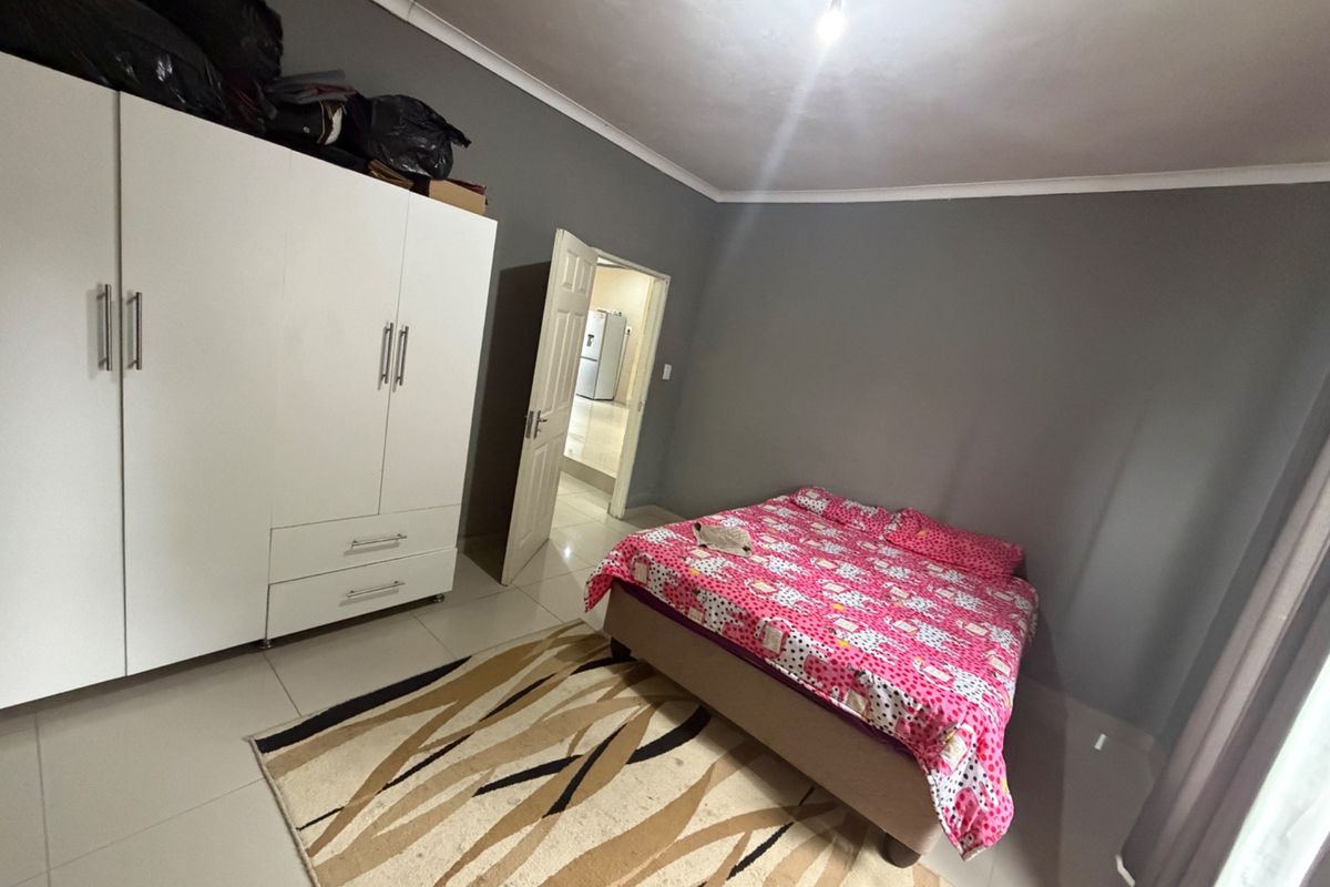 A bedroom featuring tiled flooring, a built-in wardrobe, and neutral grey walls, offering a functional space with direct access to an adjacent room.