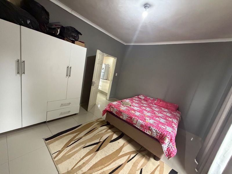 A bedroom featuring tiled flooring, a built-in wardrobe, and neutral grey walls, offering a functional space with direct access to an adjacent room.