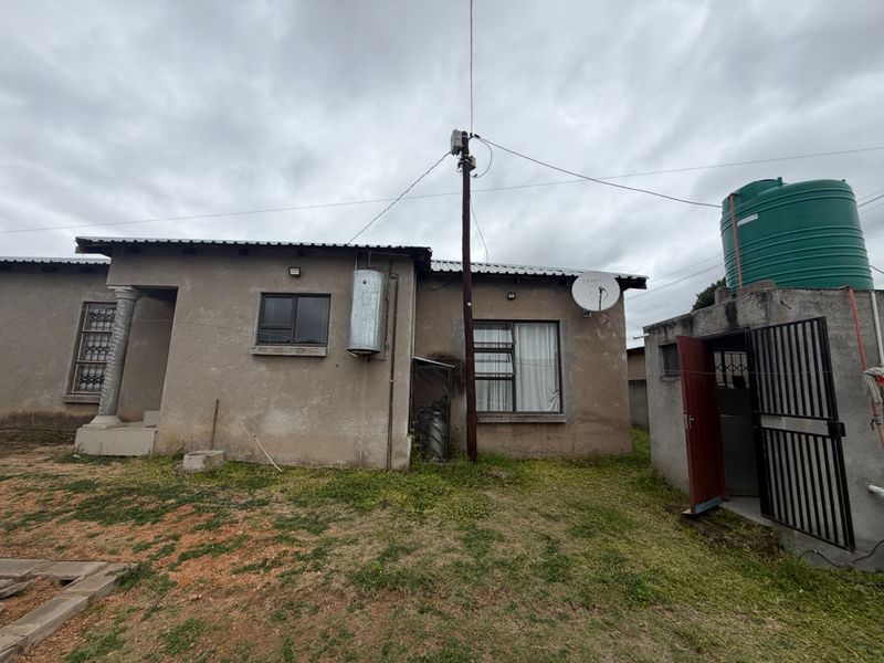 Rear view of the property featuring a corrugated metal roof, external water storage tank, and security features including window bars and a metal gate.