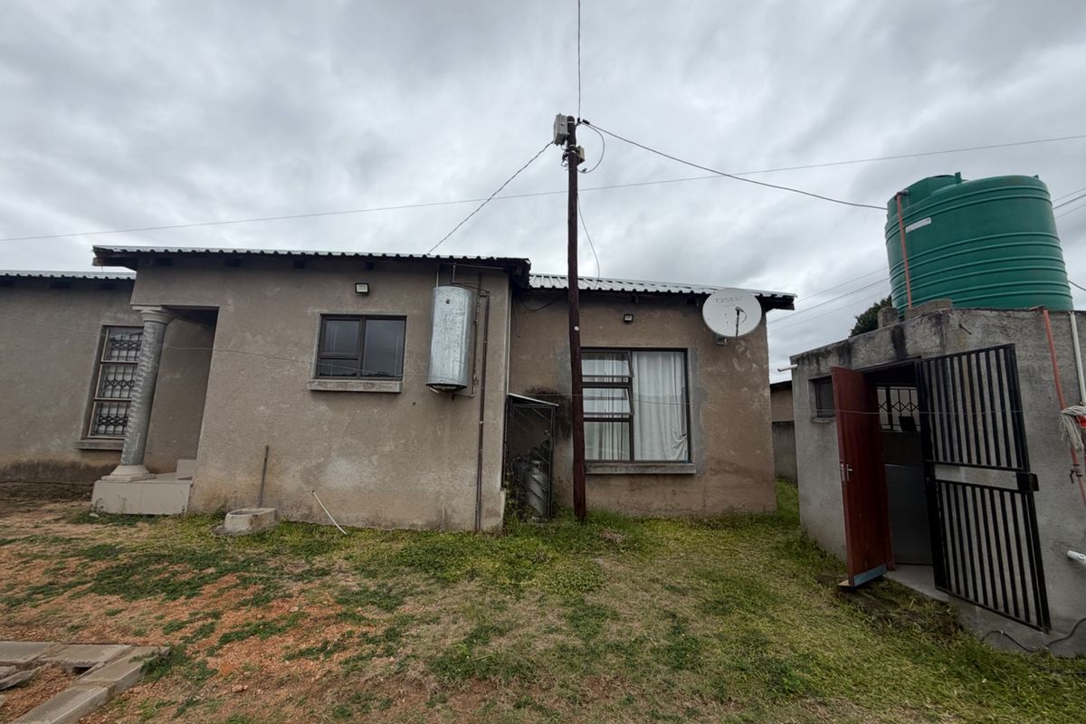 Rear view of the property featuring a corrugated metal roof, external water storage tank, and security features including window bars and a metal gate.