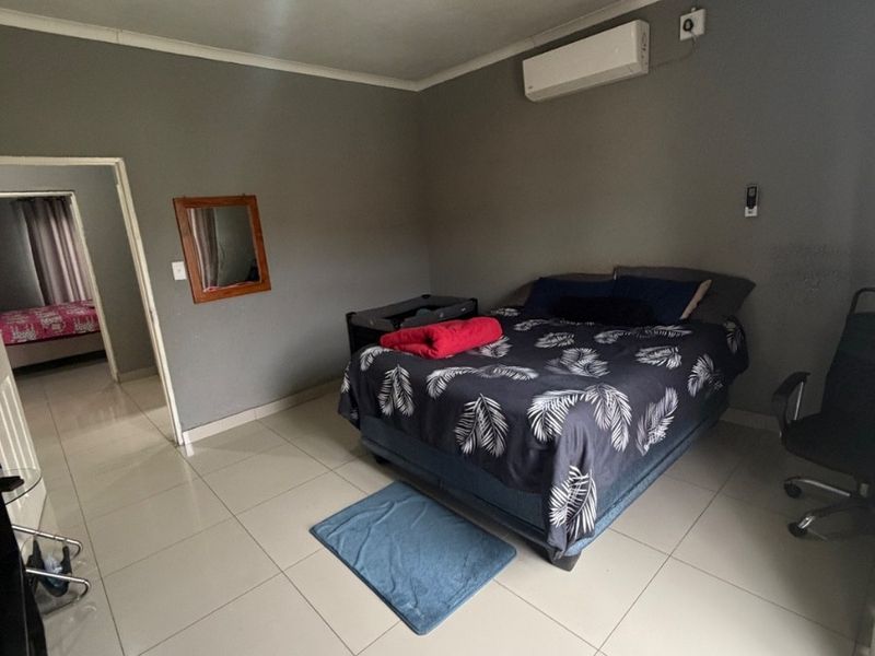 A bedroom featuring tiled flooring, a wall-mounted air conditioning unit, and neutral grey walls, providing a functional and clean living space.