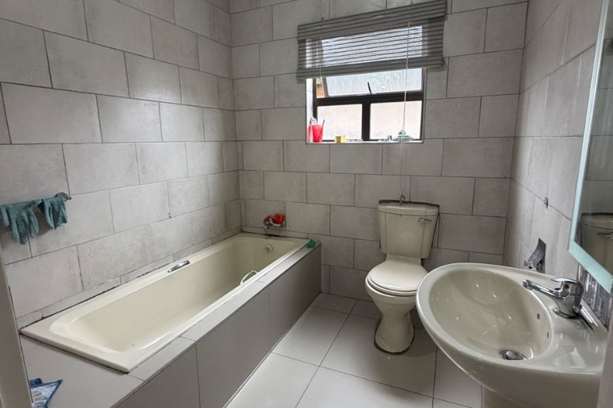 A functional bathroom featuring tiled walls and flooring, a bathtub, a pedestal basin, and a toilet, with visible signs of wear and ceiling staining.