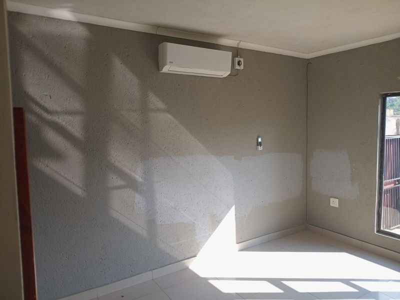 An empty bedroom featuring tiled flooring, an installed air conditioning unit, and walls requiring a fresh coat of paint for a uniform finish.
