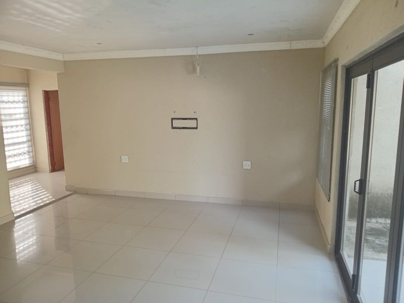 An empty, neutrally painted living room featuring tiled flooring, coving, and large sliding glass doors providing access to the exterior.