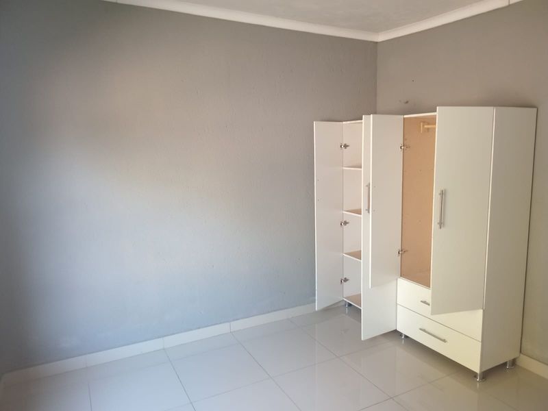 A simple, neutral bedroom featuring tiled flooring and a built-in wardrobe, offering a clean and functional space ready for personalization.