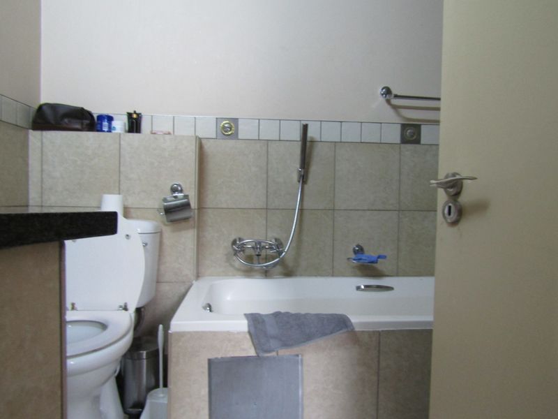 A compact bathroom featuring a bathtub with a shower mixer, a toilet, and neutral wall tiling. The bathtub side panel requires repair.