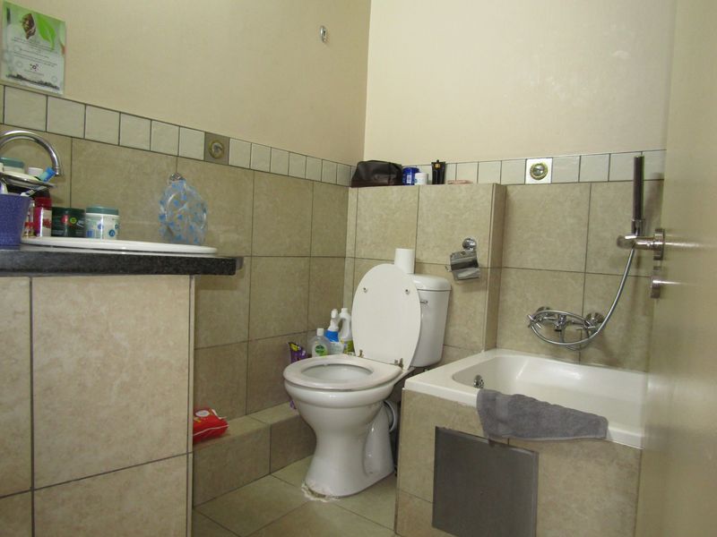 A functional bathroom featuring a built-in vanity, toilet, and a bathtub with a handheld shower mixer, finished with neutral wall and floor tiling.