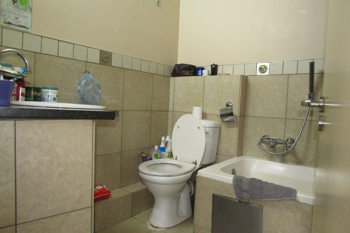 A functional bathroom featuring a built-in vanity, toilet, and a bathtub with a handheld shower mixer, finished with neutral wall and floor tiling.