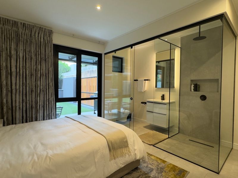 Modern bedroom featuring an integrated glass-enclosed en-suite bathroom with a wall-mounted vanity and walk-in shower, complemented by sliding door access to the patio.